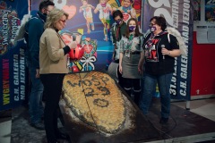 Prowadząca Monika Kosińska rozmawia z wolontariuszami. Zgromadzeni są wokół chleba w kształcie serca, ozdobionego napisem WOŚP 29. Chleb pochodzi z piekarni Dalen.