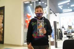 Chłopiec w ciemnej bluzie z maską WOŚP i puszką pozuje do zdjęcia przed wejściem do sklepu odzieżowego.