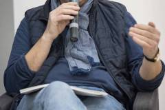 Sławomir Kuszczak siedzi w fotelu. Ubrany w pikowaną kamizelkę. Na szyi błękitna apaszka. Mówi do mikrofnu. Okulary zsunięte na nos.