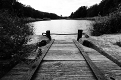 Zamknięty drewniany zjazd do jeziora. otoczonego drzewami.  Zdjęcie czarno-białe.