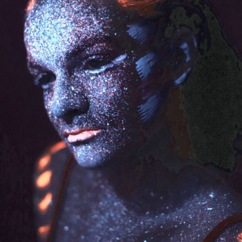 Portret kobiety w wizażu niebiesko-pomarańczowych farb UV.  Spogląda przed siebie nieobecnym wzrokiem. Ma ciasno splecione w kitkę włosy.