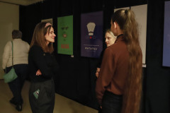 Trzy dziewczyny w trakcie rozmowy. Za nimi na czarnej kotarze wyeksponowane plakaty filmowe Maska oraz Ratutaj.