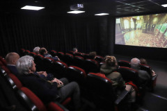 Zdjęcie zrobione z góry w małej sali kinowej. Rzędy foteli z widzami. Na ekranie wyświetlany film.