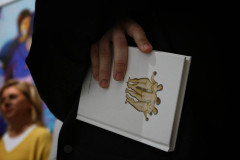 Fragment ciemnej marynarki i dłoń trzymająca książkę z reprodukcją Trzech Gracji.