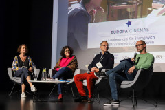 Cztery osoby na scenie zasiadają w szarych fotelach. Przed nimi stolik. W tle slajd z fragmentem napisu Europa Cinemas Konferencja Kin Studyjnych 20-22 września.