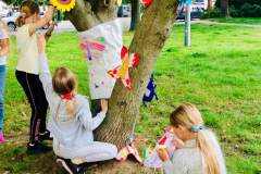 Dziewczynki dekorują drzewo pracami z papieru.