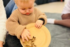 Dziecko w beżowym sweterku trzyma przed sobą przechylony papierowy talerz i zsuwa z niego foremkę w kształcie łba renifera.
