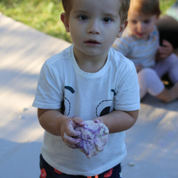 Dziecko patrzy w obiektyw. W dłoniach trzyma masę solną. Zdjęcie w planie amerykańskim.