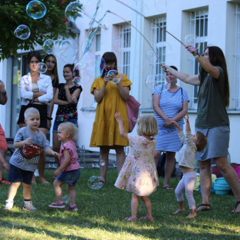 Grupa kobiet i dzieci przed budynkiekm CKiS przy Okólnej. Zabawa bańkami.