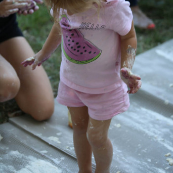 Dziewczynka w różowej koszulce z arbuzem i szortach stoi na masie. Patrzy na swoje brudne stopy.
