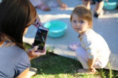 Po lewo odwrócona plecami kobieta robi zdjęcie telefonem. Po prawej kucające dziecko.