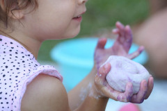 Dziewczynka sfotografowana z prawego profilu. W prawej dłoni unosi masę solną. Widać zdarte kolano.