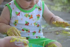 Dziecko siedzi i trzyma między nogami miskę. Ręce ma pobrudzone żółtą mazią.