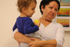 Kobieta trzyma dziecko na rękach. Dziecko trzyma żółtą piłeczkę.