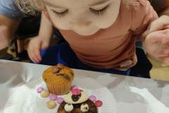Dziewczynka pochyla się nad talerzykiem z muffinką oraz misiem zrobionym z muffinki i drażetek.