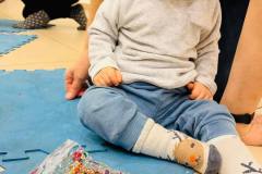 Dziecko siedzące na niebieskich puzzlach patrzy na woreczek wypełniony mazią i cekinami.