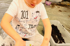 Dziewczynka w koszulce z dalmatyńczykami ugniata ziemię w doniczce z cebulką.