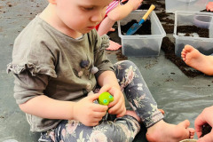 Dziecko siedzi na folii. Patrzy na doniczkę z cebulką. W dłoniach trzyma gumowego stwora.