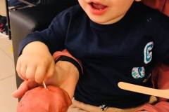 Patrzące w obiektyw dziecko wbija zapałkę w kulkę plasteliny.  W prawym dolnym rogu otwarta dłoń ze startą zapałek.