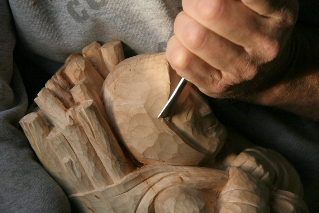 Na zdjęciu fragment rzeźby i dłoń rzeźbiarza trzymająca dłuto.